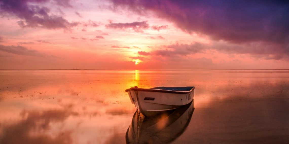 A tranquil scene of a boat at sunset with vivid sky reflecting on calm waters.