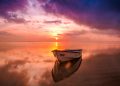 A tranquil scene of a boat at sunset with vivid sky reflecting on calm waters.