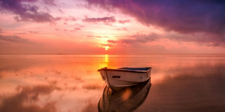 A tranquil scene of a boat at sunset with vivid sky reflecting on calm waters.