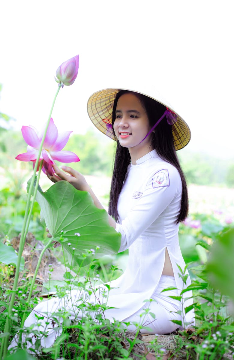 A young woman in traditional attire admires lotus flowers in a lush green field.