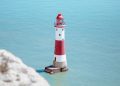 white and red lighthouse on rock formation beside body of water during daytime