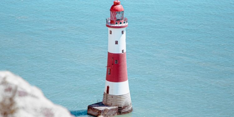 white and red lighthouse on rock formation beside body of water during daytime