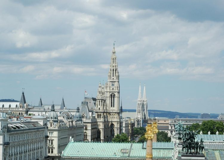 A beautiful view of Vienna's iconic architecture including the Rathaus and Votivkirche under a cloudy sky.