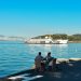 A couple enjoys the coastal view of İstanbul with a ferry in the background on a sunny day.