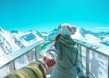 A woman in winter clothing holds a hand and walks on a scenic snow-covered mountain deck in Zell am See.
