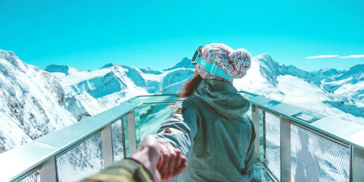 A woman in winter clothing holds a hand and walks on a scenic snow-covered mountain deck in Zell am See.