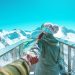 A woman in winter clothing holds a hand and walks on a scenic snow-covered mountain deck in Zell am See.