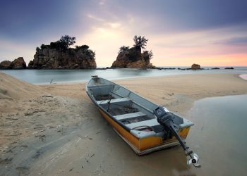 A peaceful seashore scene featuring a fishing boat on sand with a stunning dusk sky.