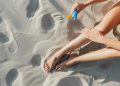 Close-up of a woman's legs as she applies sunscreen on a sunny beach day.