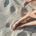 Close-up of a woman's legs as she applies sunscreen on a sunny beach day.
