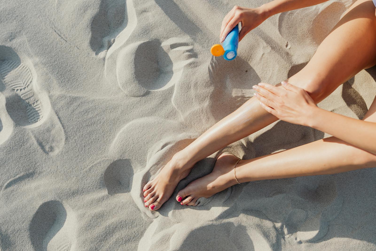 Close-up of a woman's legs as she applies sunscreen on a sunny beach day.