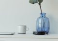 Elegant minimalist desk with blue vase, eucalyptus, mug, and laptop on a white table.