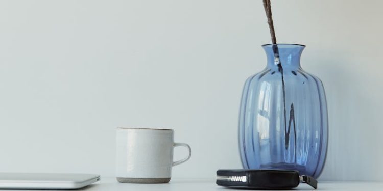 Elegant minimalist desk with blue vase, eucalyptus, mug, and laptop on a white table.