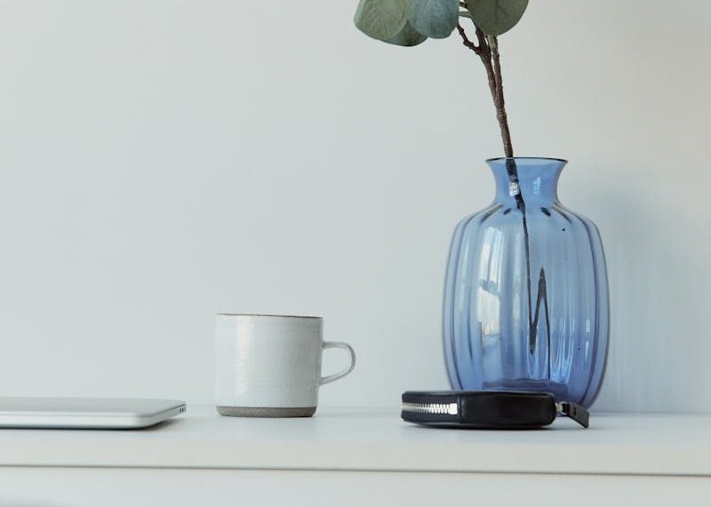 Elegant minimalist desk with blue vase, eucalyptus, mug, and laptop on a white table.