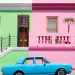 blue sedan parked beside pink and green house