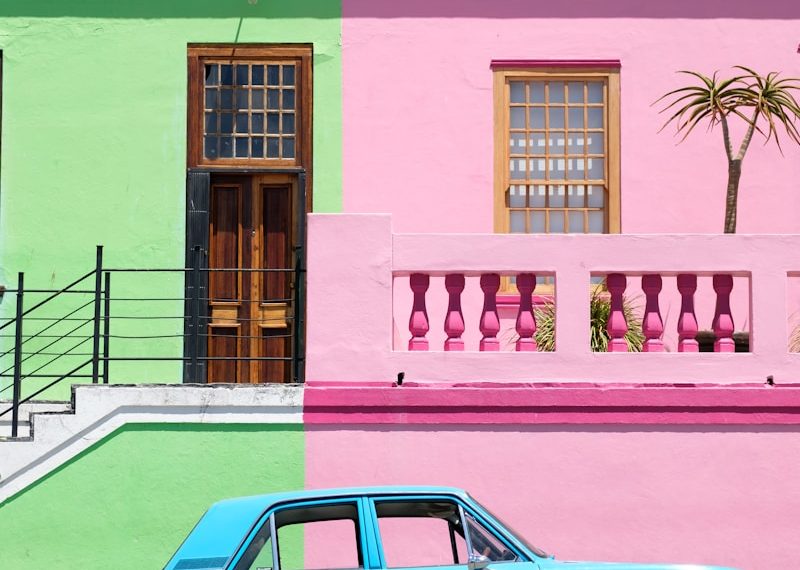 blue sedan parked beside pink and green house