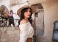 woman in white off shoulder long sleeve shirt and brown hat standing near brown concrete wall
