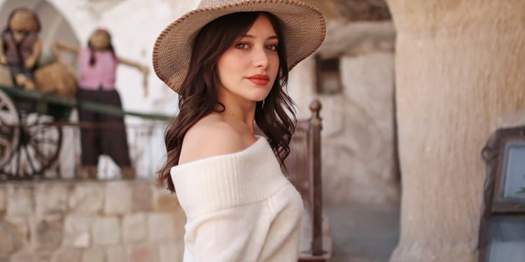 woman in white off shoulder long sleeve shirt and brown hat standing near brown concrete wall
